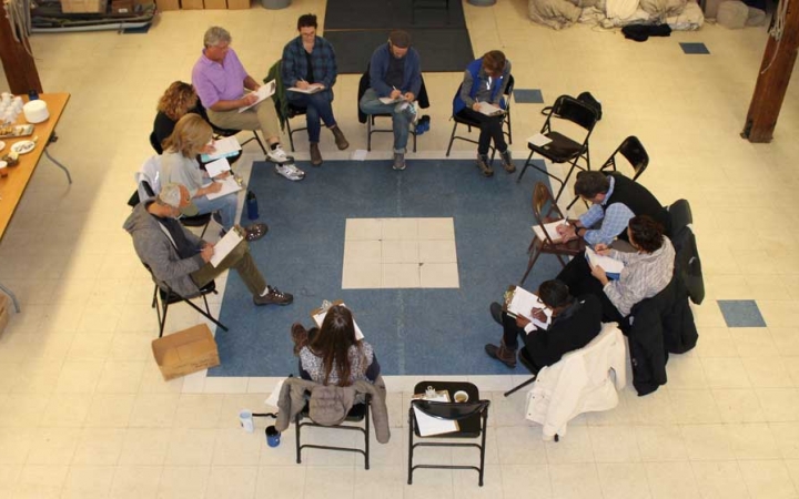 A group of people sit in chairs arranged in a circle during the family seminar of an outward bound intercept course.